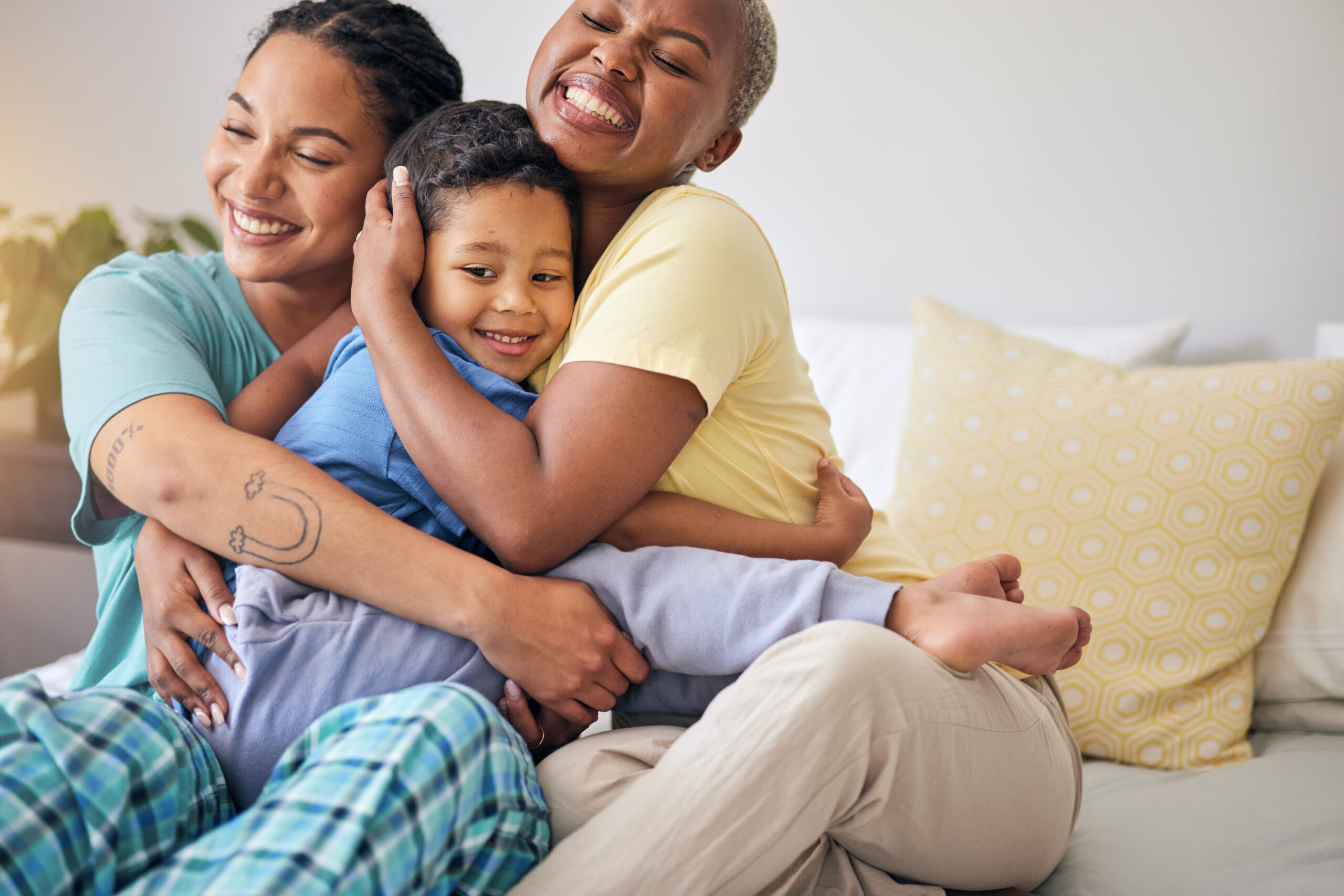 LGBT, bedroom hug and happy family, child and relax mothers bonding, support and enjoy quality time together. Home, care and gay people, homosexual parents or lesbian women embrace young kid on bed